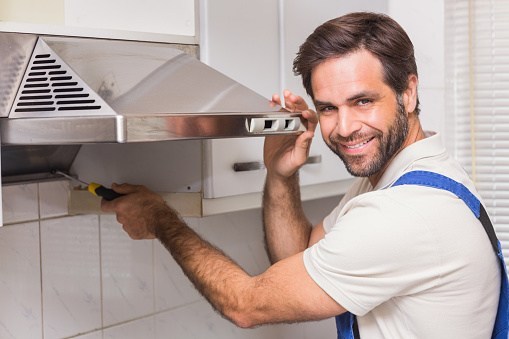 Smiling technician repairing a range hood fan in a Winnipeg home