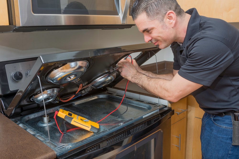 Appliance technician testing a stove and cooktop with a multimeter in Winnipeg